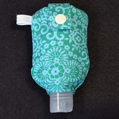 a green and white flowered bottle cover on a black surface with a button in the middle