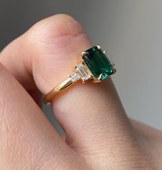 a woman's hand holding an emerald and diamond ring on her left side, with the other half in yellow gold