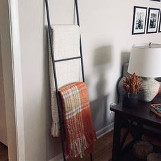 a ladder leaning against the wall next to a table with a lamp and pictures on it