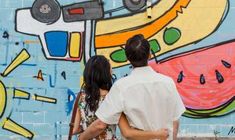 a man and woman are standing in front of a wall with colorful art on it