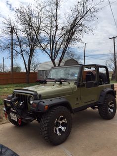 a green jeep parked on top of a parking lot next to a house and trees