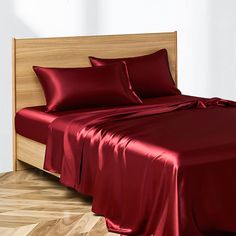 a bed with red sheets and pillows on top of wooden headboard next to hardwood flooring