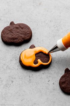 a cookie being decorated with orange icing and chocolate cookies next to it are shaped like an elephant