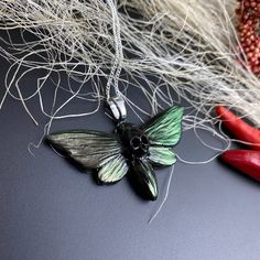 a green and black butterfly on a chain next to some red scissors with white hair