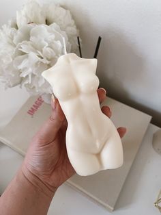 a hand holding a small white object next to a vase with flowers in it on a table