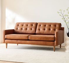 a brown leather couch sitting on top of a white rug next to a vase with flowers