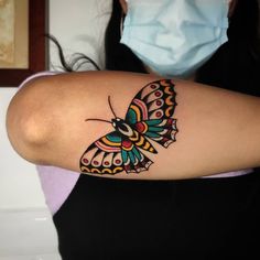 a woman wearing a face mask with a butterfly tattoo on her left arm and shoulder