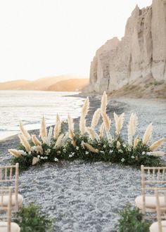 an outdoor ceremony setup with chairs and flowers on the sand near the water's edge