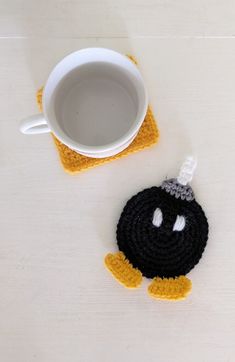 a crocheted coffee cup holder with a smiley face on it next to a mug