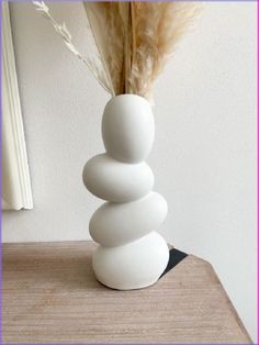 a white vase sitting on top of a wooden table next to a feather in it