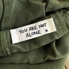 a label that says you are not alone on the back of a green shirt with white writing