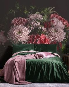 a bed with green sheets and pink flowers on the headboard, in front of a black wall