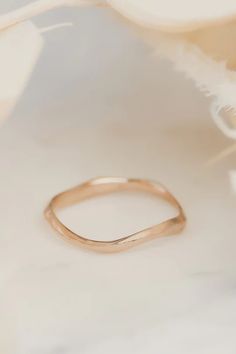 a gold wedding band sitting on top of a white marble table next to a flower