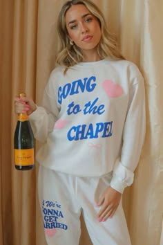 a woman holding a bottle of wine in her right hand and wearing pajamas that say going to the chapel