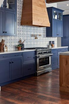 a kitchen with blue cabinets and wood flooring is pictured in this image, there is a range hood over the stove