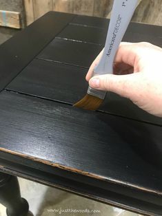 a hand holding a paint brush over a black wooden table with white writing on it