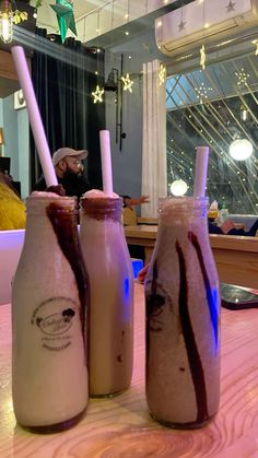 two milkshakes sitting on top of a table with straws in each bottle