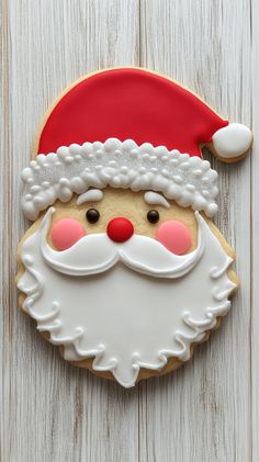 a decorated christmas cookie with santa claus's hat and beard on the top, sitting on a white wooden surface