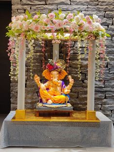 a statue of the god ganesh in front of a stone wall with flowers on it