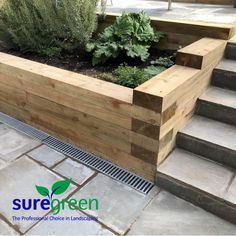 a wooden planter filled with lots of plants on top of cement flooring next to steps