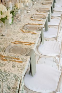 the table is set with white chairs and place settings for several people to sit at