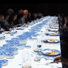 a group of people sitting at a long table with plates and wine glasses on it