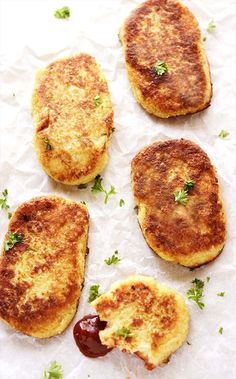 four crab cakes with ketchup and parsley on top sitting on wax paper