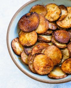 a bowl filled with fried potatoes on top of a blue tablecloth and white surface