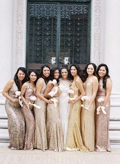 a group of women standing next to each other in front of a building wearing gold dresses