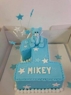 a blue birthday cake with white stars and a teddy bear on the top, sitting in a box