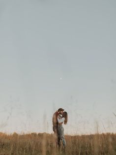 a man and woman kissing in the middle of a field with tall grass on either side