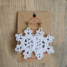 two crocheted snowflakes hanging from hooks on a wooden surface with a tag