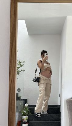 a pregnant woman taking a selfie with her cell phone while standing on the stairs