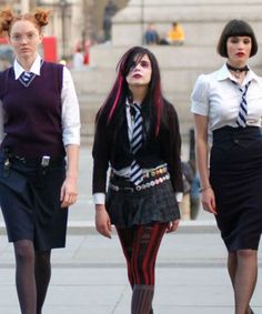 three young women dressed in school uniforms walking down the street with their hair pulled back