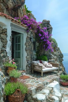 a stone house with potted plants and flowers on the front porch, overlooking the ocean