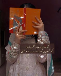 a woman holding an orange book in front of her face with arabic writing on it