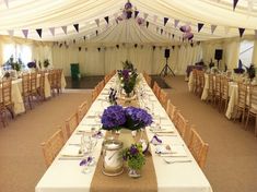 the tables are set up with purple flowers in vases and silverware on them