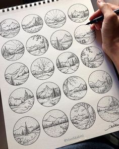 a person is holding a pen and drawing pictures on a sheet of paper with mountains in the background