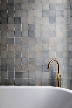 a white bath tub sitting next to a wall covered in gray tiles and a faucet