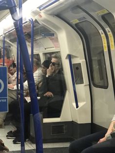 people are sitting on the subway train and one person is talking on his cell phone