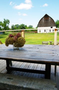 a wooden table sitting on top of a wooden deck next to a barn and field