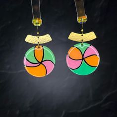 a pair of colorful earrings hanging from hooks on a black background with light coming through