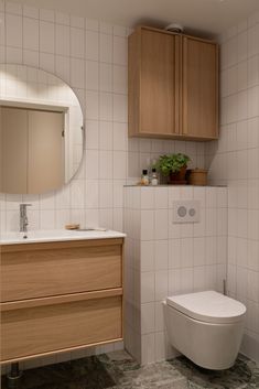 a white toilet sitting next to a wooden cabinet in a bathroom under a round mirror