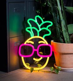 a neon pineapple with sunglasses is sitting next to a potted plant and some plants