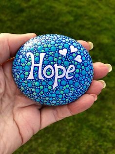 a hand holding a painted rock with the word hope written on it and hearts in white