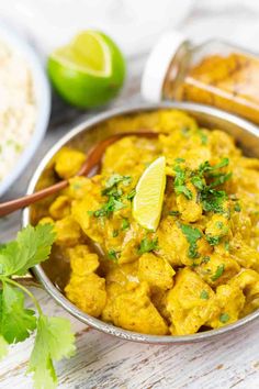 a metal bowl filled with chicken curry next to rice and cilantro wedges