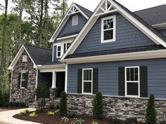 a blue house with black shutters and white trim on the windows, along with landscaping