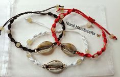 three bracelets with seashells and beads on white cloth covered napkin next to glass bag