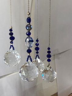 three blue and clear glass beads hanging from a metal chain on a white wall next to a window