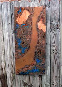 a rusted metal piece hanging on a wooden fence next to a brick wall with blue and orange paint